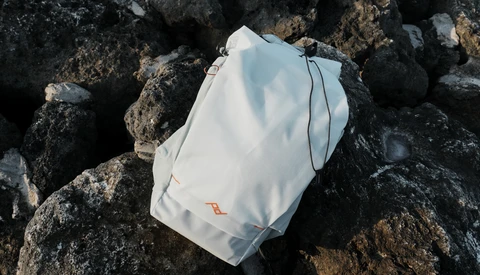White drawstring bag with orange accents resting on dark, weathered rocks.