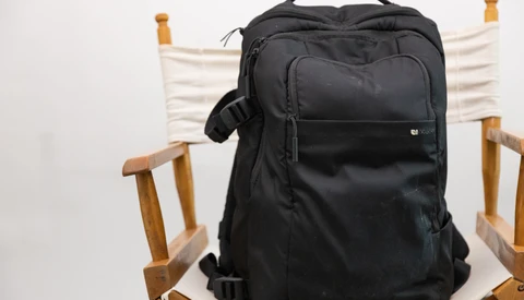 Black camera backpack displayed on a wooden chair with white canvas seat and back.