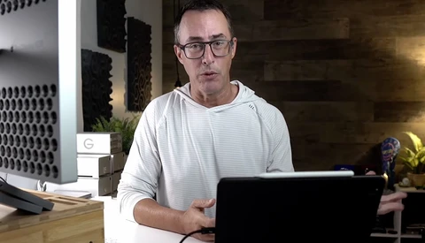 Man wearing glasses working at laptop in modern office space with ambient lighting.