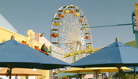 Ferris wheel with yellow and orange gondolas framed by blue tent canopies in foreground.