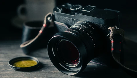 Vintage rangefinder camera with manual lens and yellow filter on dark surface.