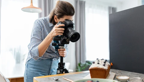 Photographer using a telephoto lens mounted on a tripod while shooting a styled food scene indoors.