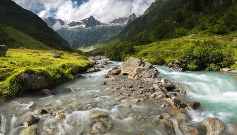 Turquoise river flowing through an alpine valley with snow-capped peaks and lush green meadows.