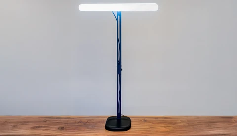 Modern desk lamp with tall dark blue-black stand and white LED panel on wooden surface.
