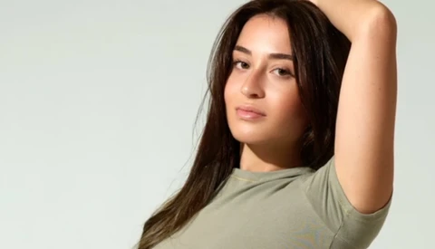 Woman with long dark hair in casual pose against neutral background.