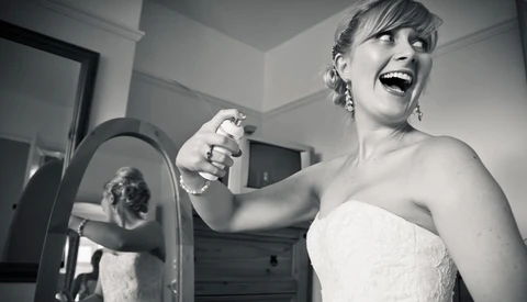 Bride in strapless wedding dress smiling while holding handheld mirror in black and white portrait.