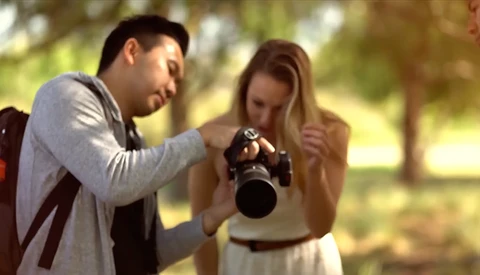 Male photographer showing a female subject a photo on the back of his DSLR camera outdoors.