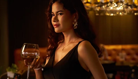 Woman in black dress holding wine glass with warm golden lighting in background.