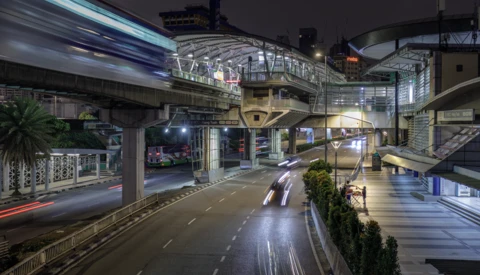 Nighttime urban street scene with elevated highway overpass, wet pavement, and blurred vehicle lights.