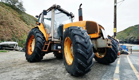 Yellow and black agricultural tractor with large treaded tires parked on a paved road near hillside terrain.
