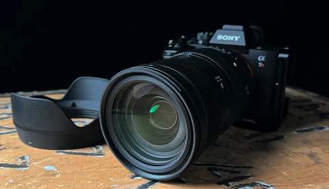 Sony mirrorless camera with attached lens and shoulder strap on textured wooden surface.
