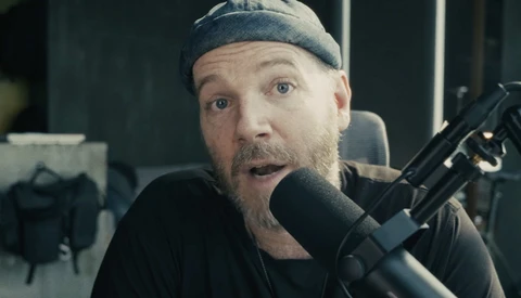 Person speaking into a large-diaphragm microphone in a studio setting with surprised expression.