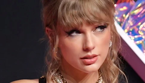 Close-up portrait of a woman with blonde hair and bangs, wearing dramatic makeup and gold chain necklace.