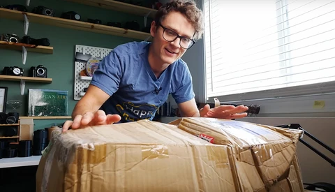 Photographer unwrapping a large brown cardboard package in a bright studio workspace.