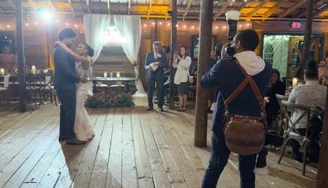Bride and groom first dance at indoor wedding reception with guests watching from wooden floor venue.