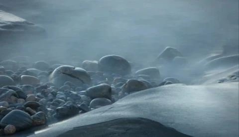 Snow-covered boulders shrouded in mist along a frozen coastline.