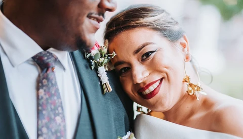 Bride and groom smiling closely together, with bride wearing red lipstick and gold earrings.