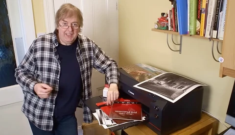 Photographer displaying printed photographs and photo book next to a desktop printer.