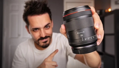 Photographer holding a Canon RF 35mm lens toward the camera in an indoor studio setting.