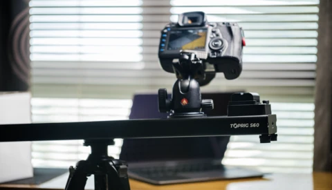 DSLR camera mounted on a Toprig 560 slider with a tripod head, positioned in an indoor studio setting with bright window backlighting.