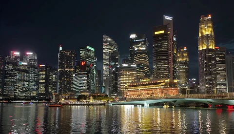 Illuminated downtown skyline reflected in calm water at night with bridge in foreground.