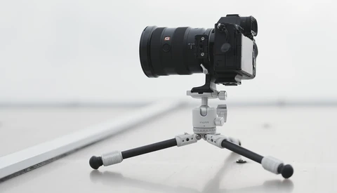 Mirrorless camera with telephoto lens mounted on a compact tripod against a minimalist gray background.