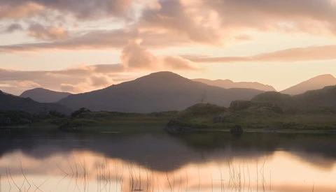 Mountain landscape reflected in still water at golden hour with warm, diffused light.