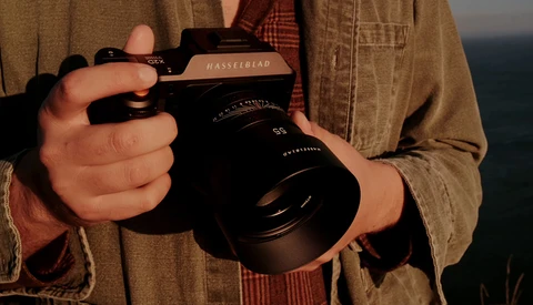 Photographer holding a Hasselblad camera with a large lens, wearing a tan button-up shirt.
