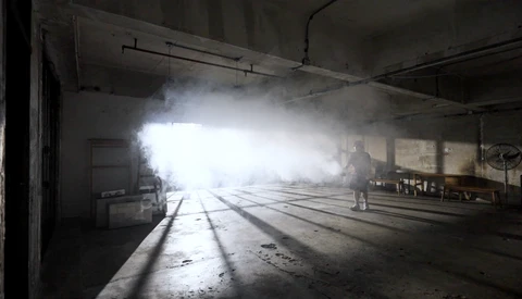 Dramatic light beam streaming through abandoned warehouse interior with concrete floor and industrial ceiling.