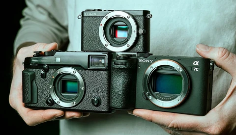 Three mirrorless cameras held in hands, showing sensor sizes from smallest to largest.