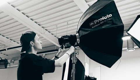 Photographer adjusting a large black Profoto softbox mounted on a light stand in a studio with white ceiling.