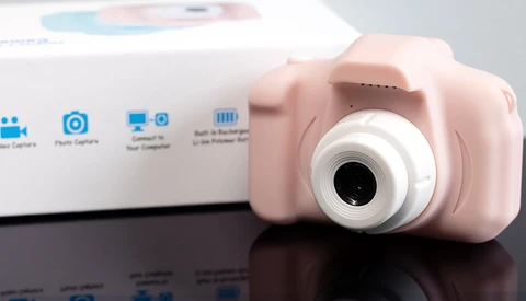 Pink compact digital camera with white lens barrel displayed next to its product packaging box.