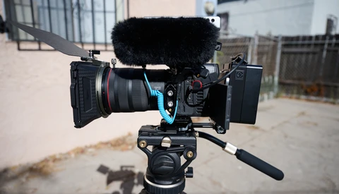 Professional cinema camera rig with follow focus wheel and shotgun microphone mounted on tripod.
