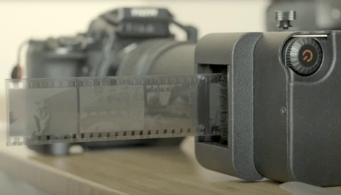 Compact digital camera next to 35mm film roll and vintage film camera in soft studio lighting.