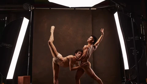 Two dancers in a studio performing a contemporary lift against a brown backdrop with professional lighting.
