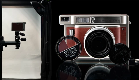 Vintage instant camera in red and chrome with accessories on reflective black surface.