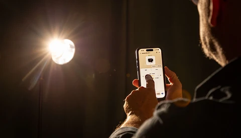 Photographer holding smartphone while composing a shot of a bright studio light fixture.