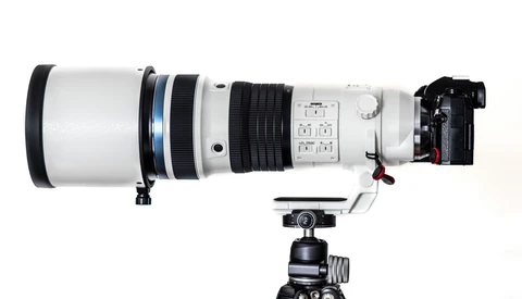 White telephoto lens mounted on tripod with ball head and camera body attached.