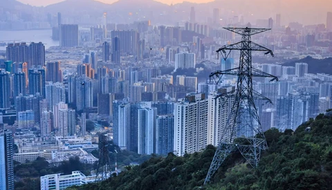 High-voltage transmission tower overlooking a sprawling cityscape at dusk with mountains in the distance.