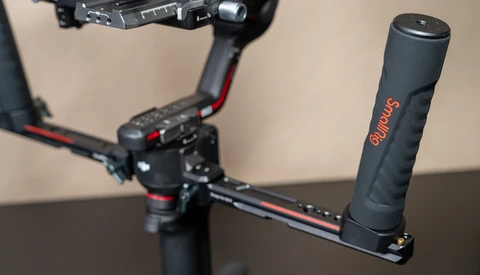 Gimbal stabilizer with extended arm grip mounted on table, with motorized gimbal head visible in background.