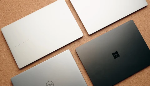 Four laptop computers arranged on a cork surface, showing their closed lids from above.