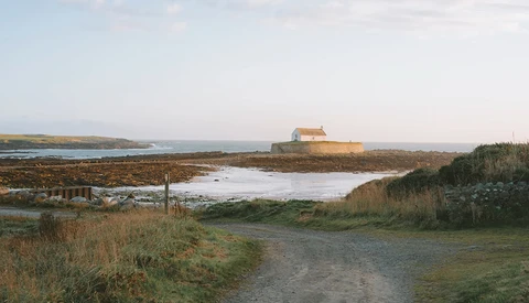 Isolated stone building with orange roof on distant headland overlooking tidal marshland and mudflats.