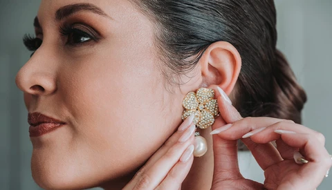 Woman in profile adjusting a pearl and crystal cluster earring near her ear.