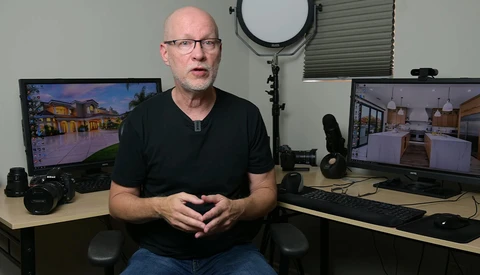 Man in black shirt seated at desk with dual monitors displaying architectural renderings.