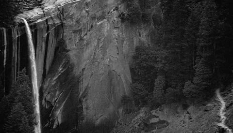 Waterfall cascading down a rocky cliff face surrounded by dense forest in black and white.