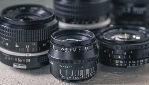 Three vintage manual focus lenses with aperture and focus rings visible, arranged on a neutral surface.