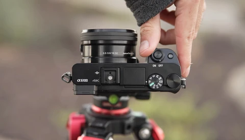 Sony a6100 mirrorless camera held in hand with attached lens, showing top controls and 4K capability marking.