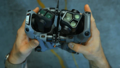 Overhead view of hands holding a drone remote controller with dual control sticks and illuminated button interface.