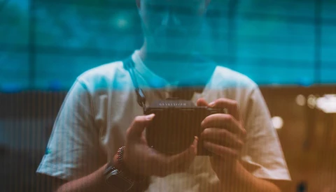 Photographer holding a vintage camera with blue-tinted window reflections obscuring their face.
