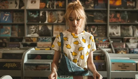 Woman wearing a taco-print t-shirt standing in front of a record store display wall.